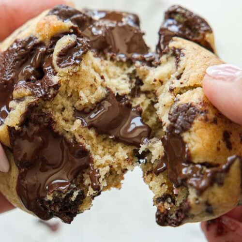 Close-up of hands pulling apart a warm, gooey vegan chocolate chip cookie, with melted chocolate oozing from the center.
